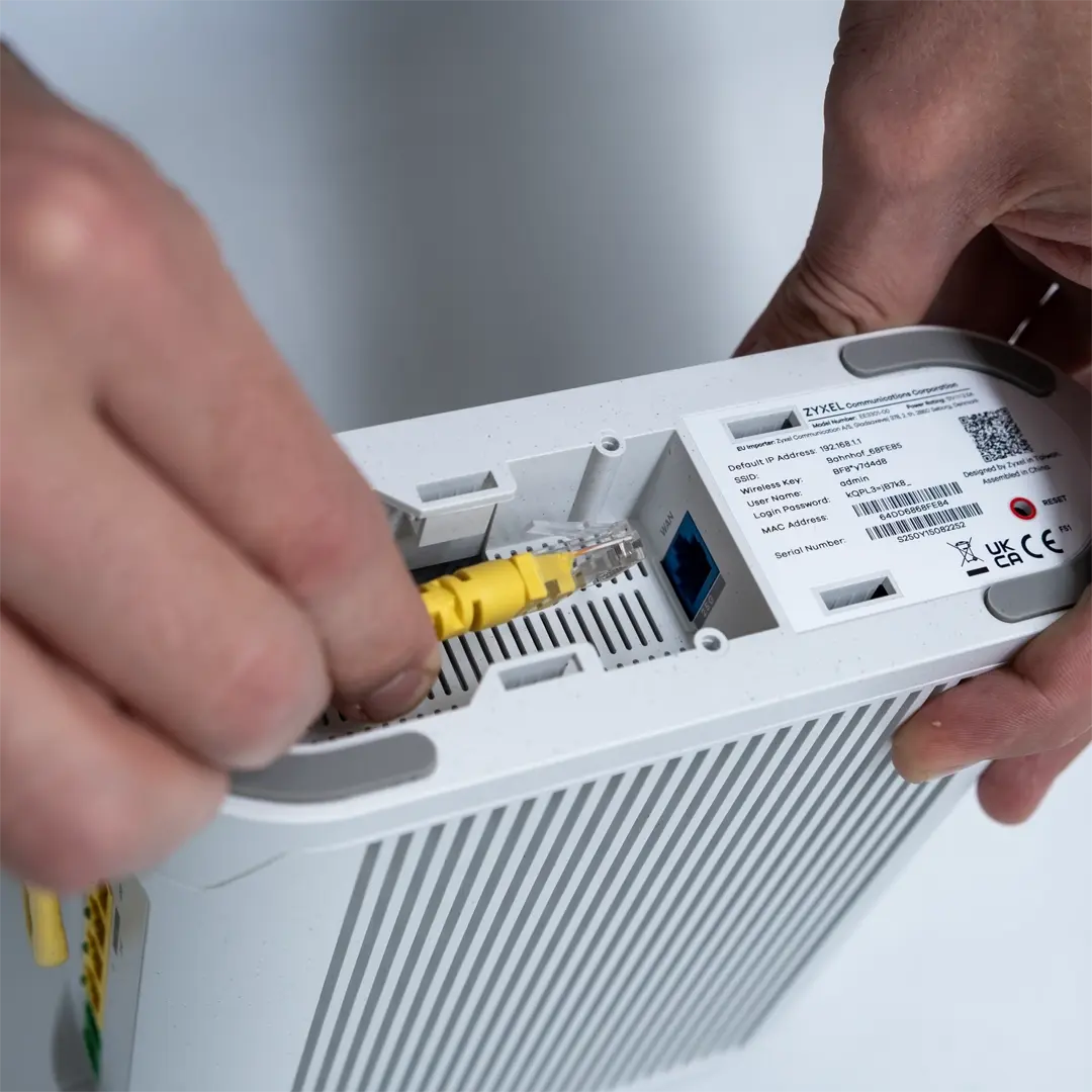 En person tilslutter et gult netværkskabel til porten på undersiden af en Zyxel-router.