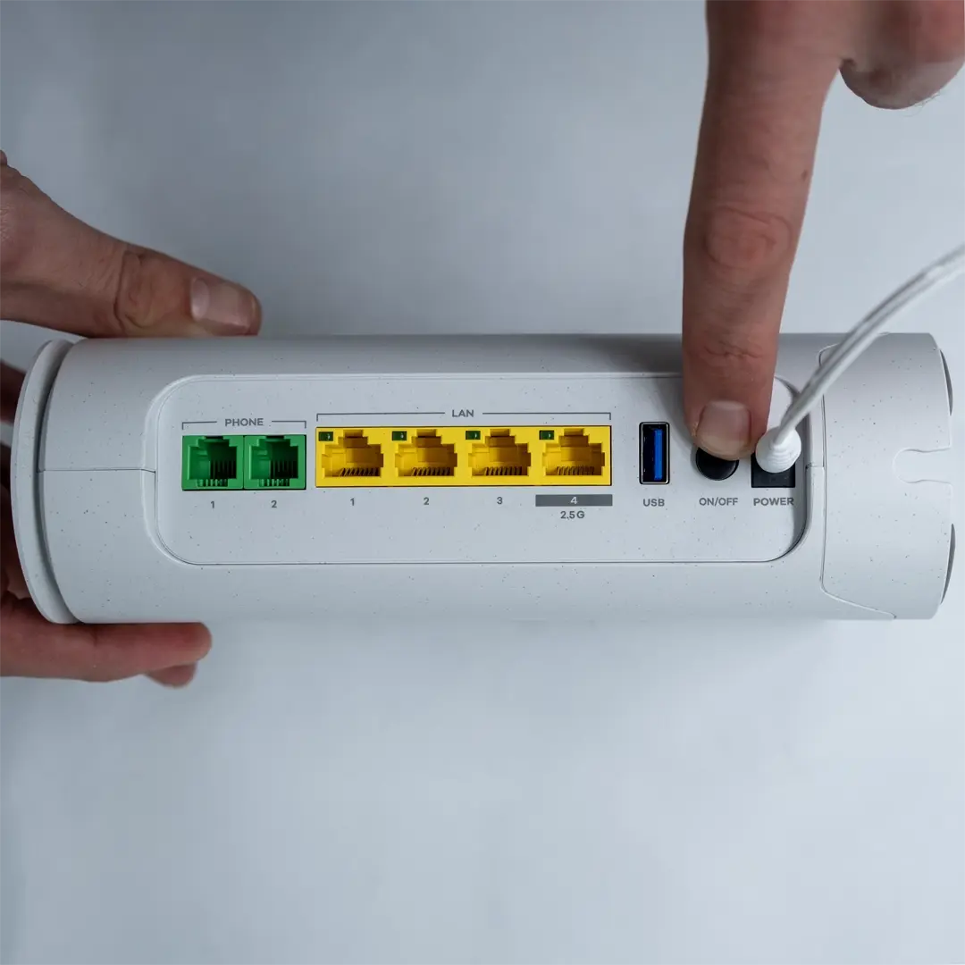 En person holder en Zyxel-router og har tilsluttet et gult netværkskabel til porten på undersiden af enheden.