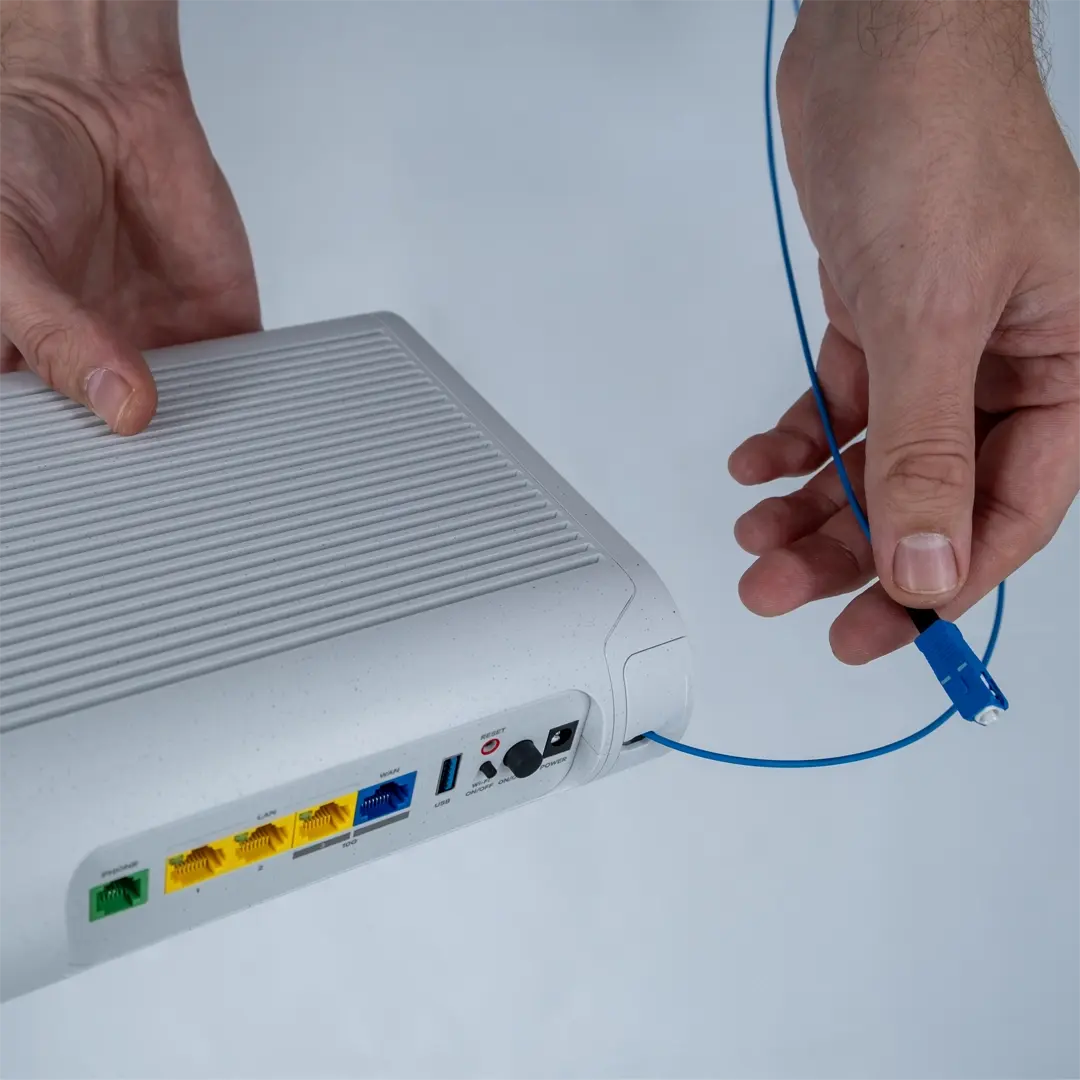 En person trykker på tænd/sluk-knappen på bagsiden af en router efter at have tilsluttet strømkablet til stikket.