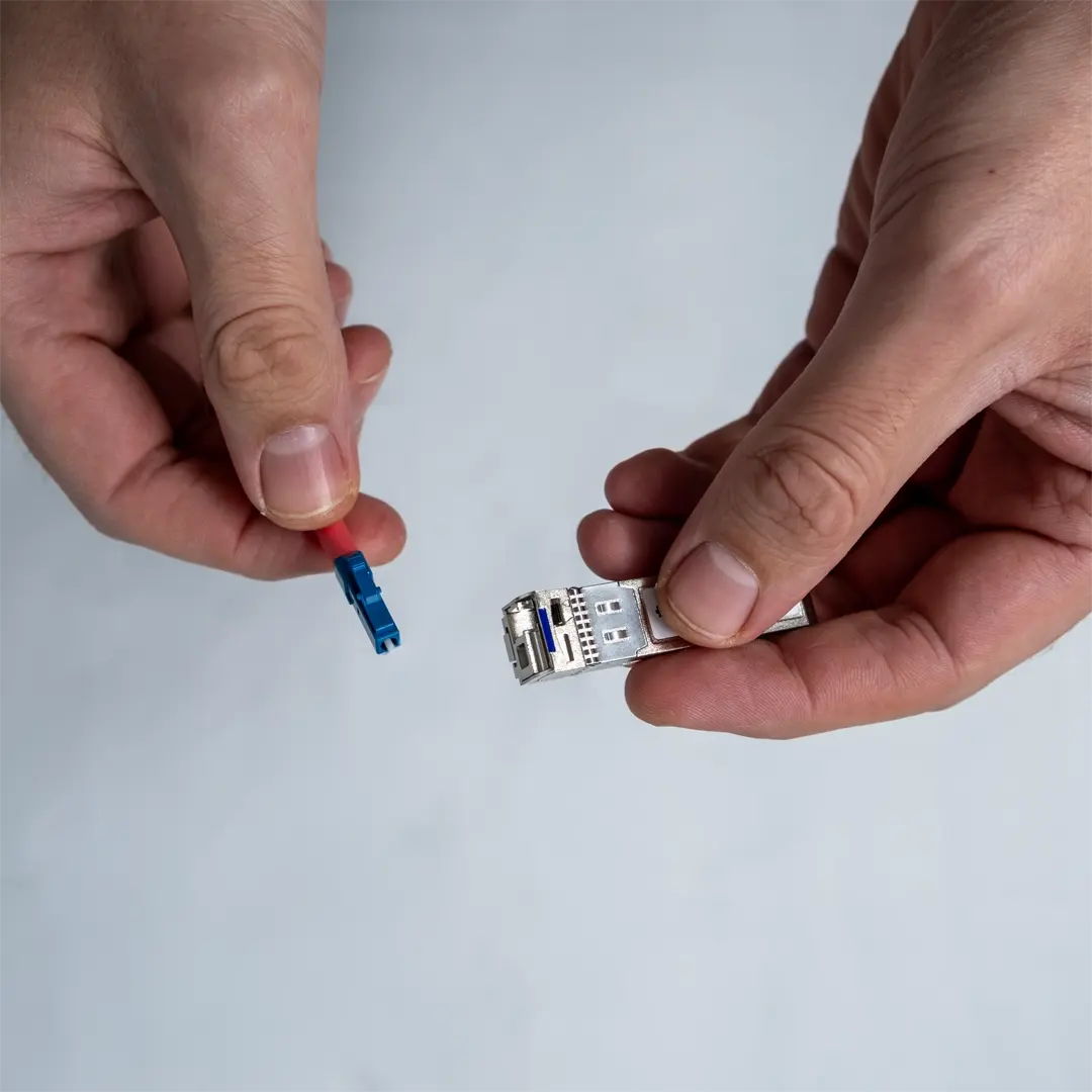 En person holder et SFP-modul i den ene hånd og viser stikket på det blå fiberkabel i den anden.