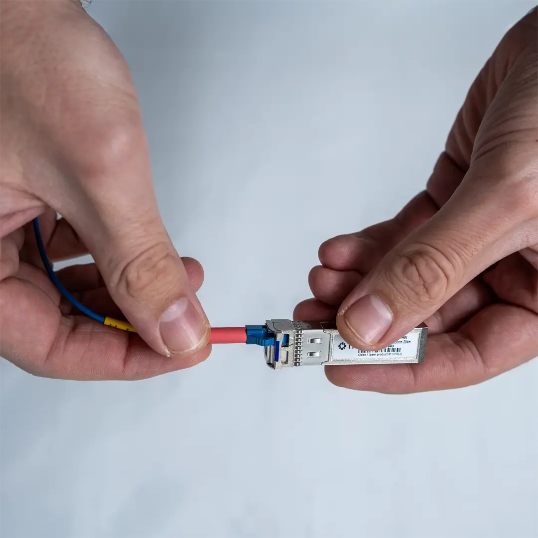 En person tilslutter et blåt fiberkabel til et SFP-modul ved forsigtigt at føre stikket ind, indtil det sidder fast.