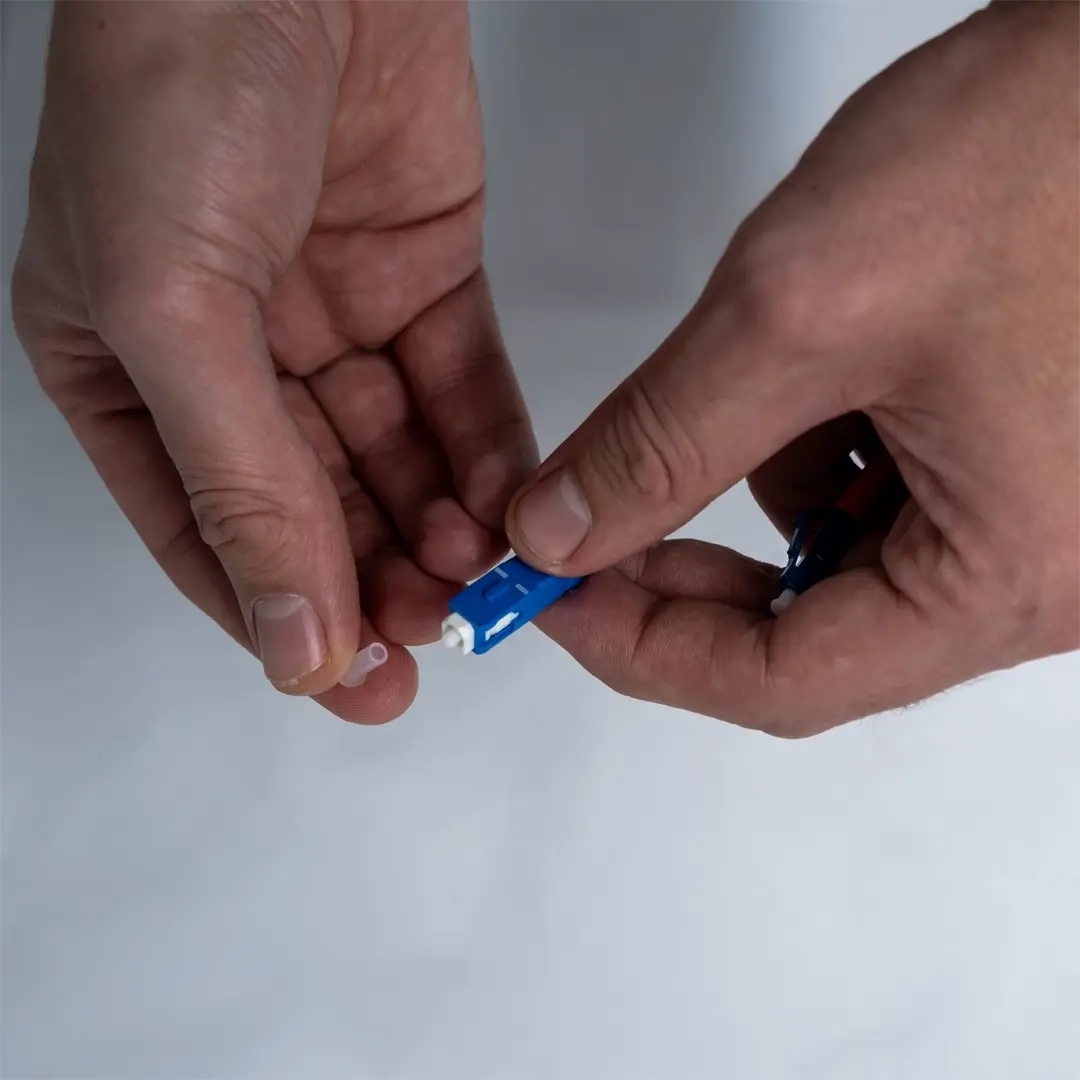 En person fjerner den gennemsigtige beskyttelseshætte fra enden af et blåt fiberkabel.