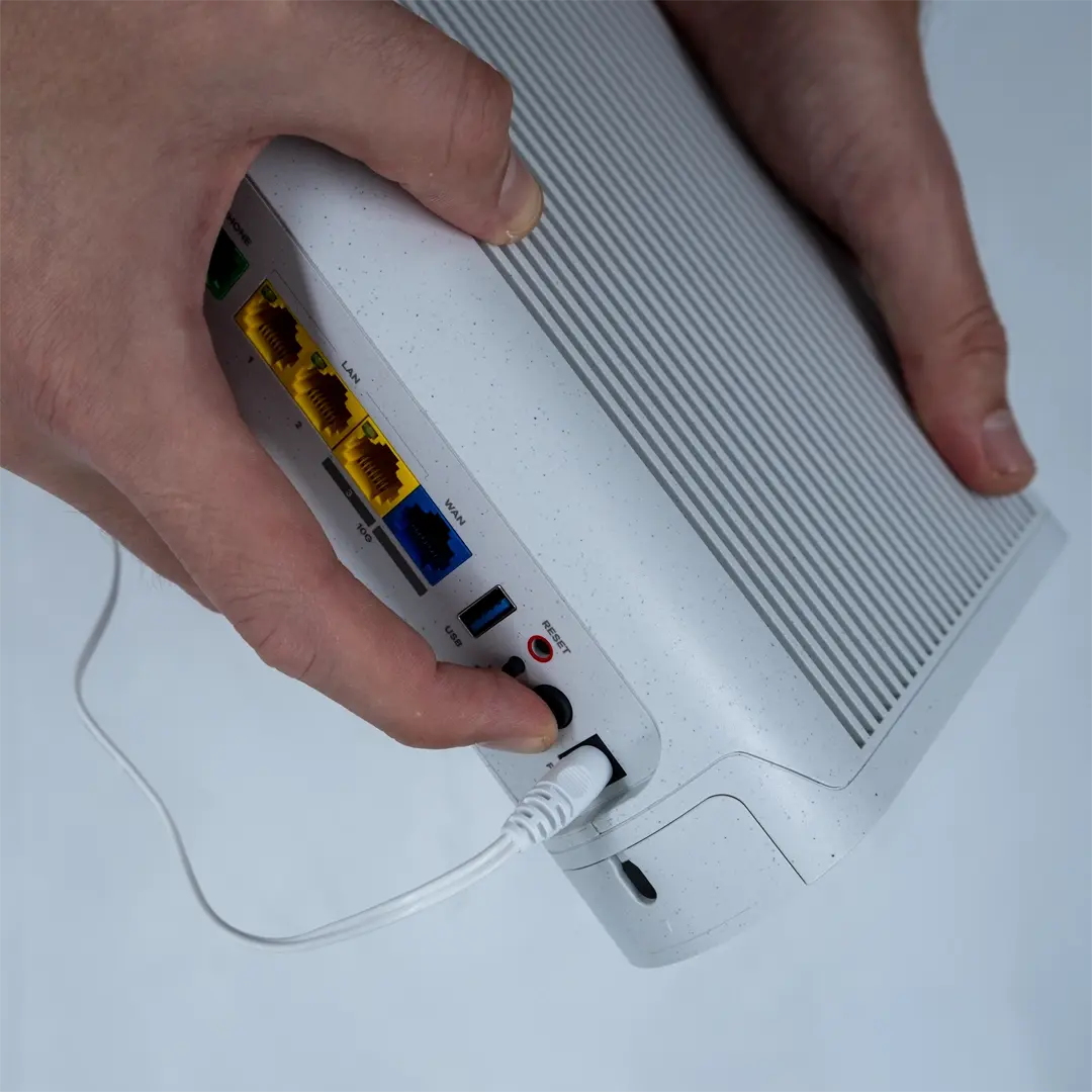 En person trykker på tænd/sluk-knappen på bagsiden af en router, efter at have tilsluttet strømkablet til stikket.