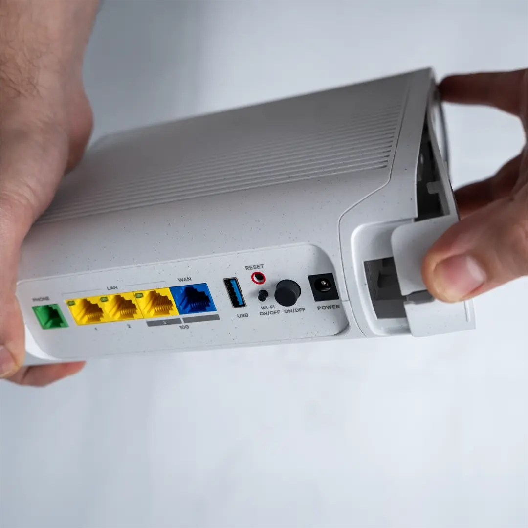 En person fjerner forsigtigt bundlåget på routeren ved at trække i kanten.