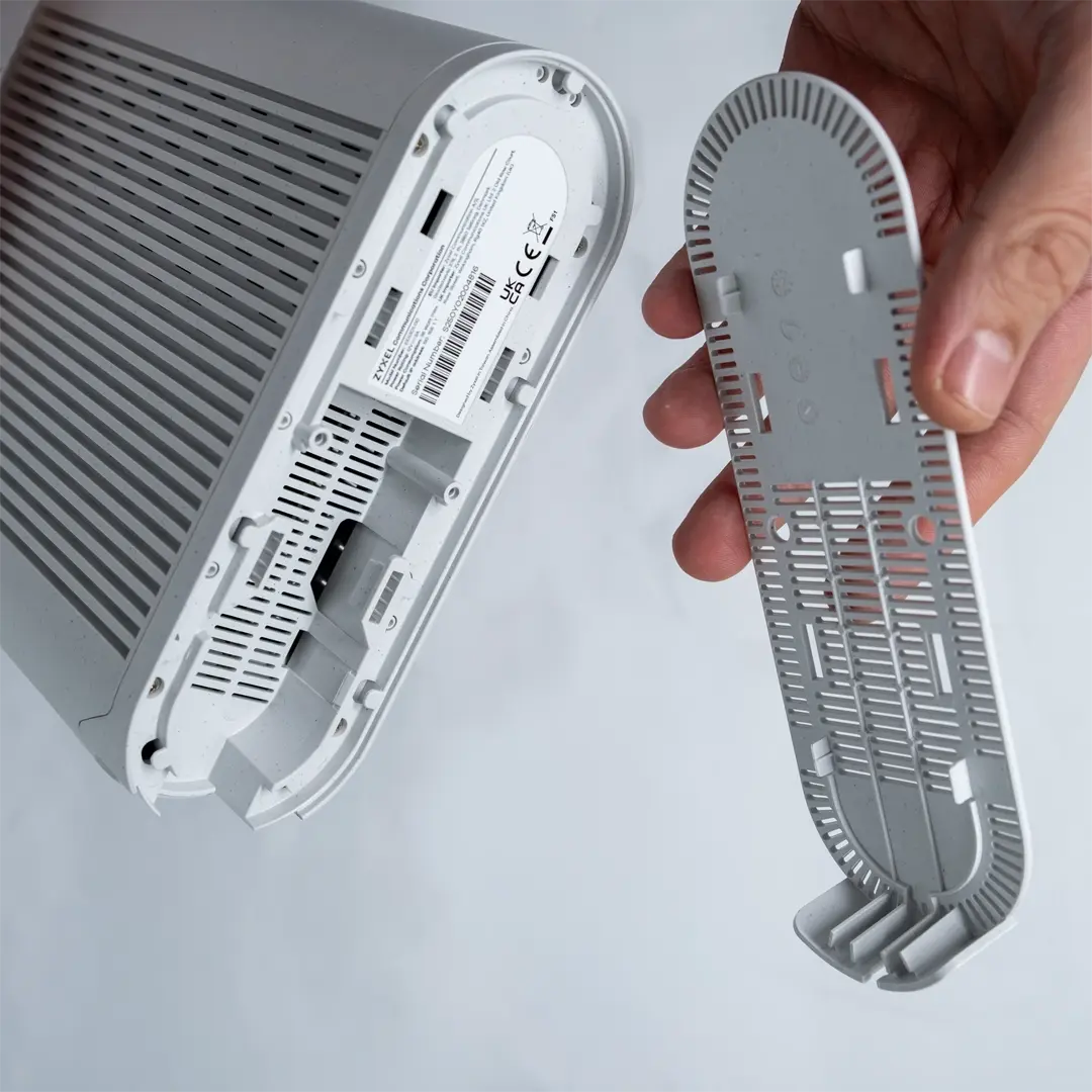 En person har fjernet bundlåget fra en router og holder det ved siden af enheden, så portene på undersiden er synlige.